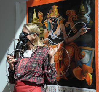 Johanna Poethig models a futuristic device; her painting shows the same device being merged with a futuristic religious culture in the form of the Hindu God Ganesh.